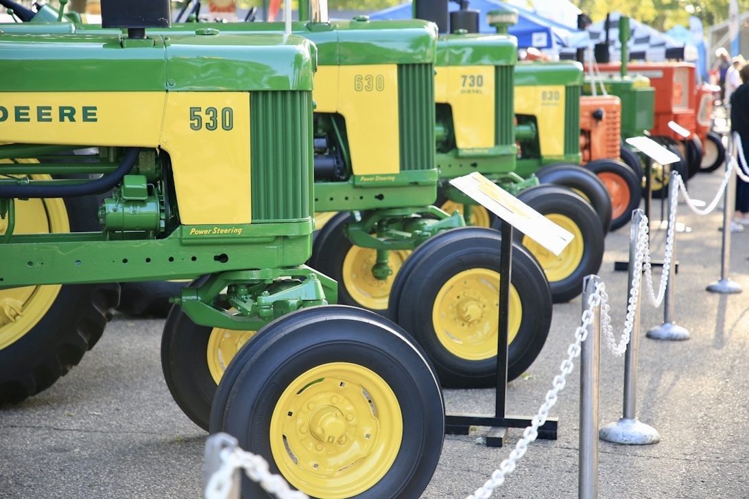 En rad med äldre John Deere-traktorer uppställda för visning på en auktion.